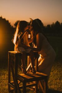 A woman and child share a tender moment during sunset, holding a lantern.