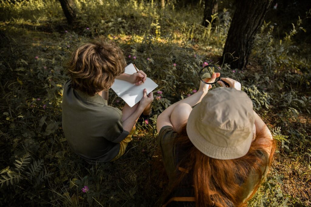 Two kids explore a forest, observing nature with a sketchbook and magnifying glass.