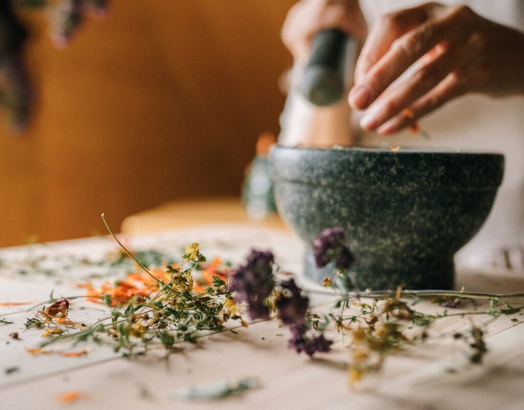 Close-up of hands using mortar and pestle to grind dried flowers on wooden table.