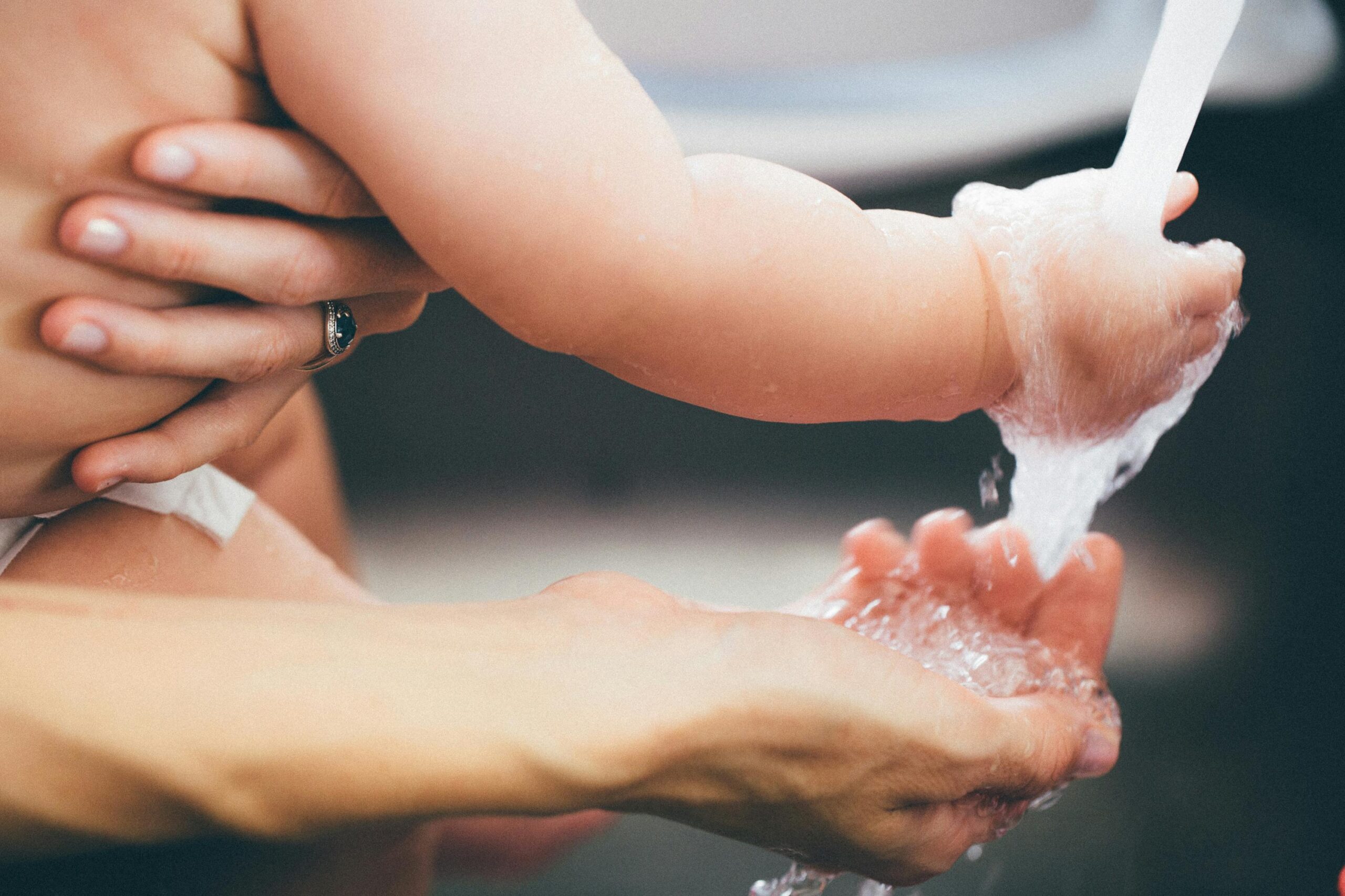 mother gently washing baby's feet under running water, bathing baby naturally